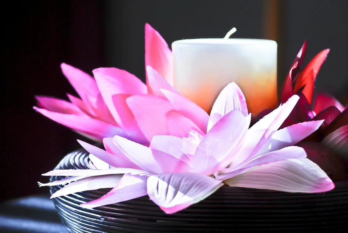 A candle and pink flower on a black plate.